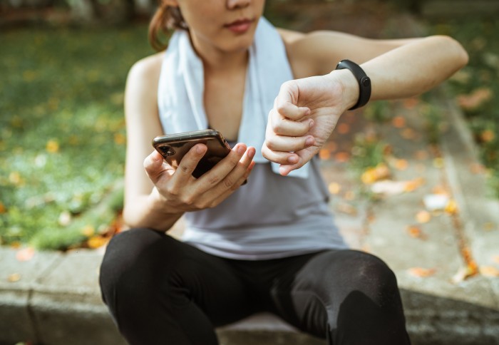 Woman in exercise clothes looking at her watch and holding a phone