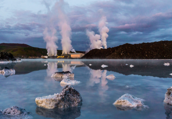 Photo of Svartsengi Geothermal Power Plant in Iceland steaming massively with reflection in a blue water of geothermal pool after the sunset and dramatic blue violet sky with thick clouds