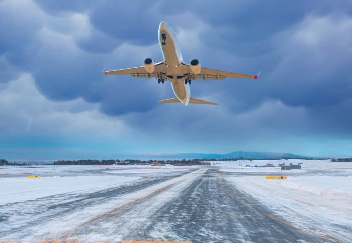 Photo of plane taking off from a white, icy runway against a bright blue but cloudy sky