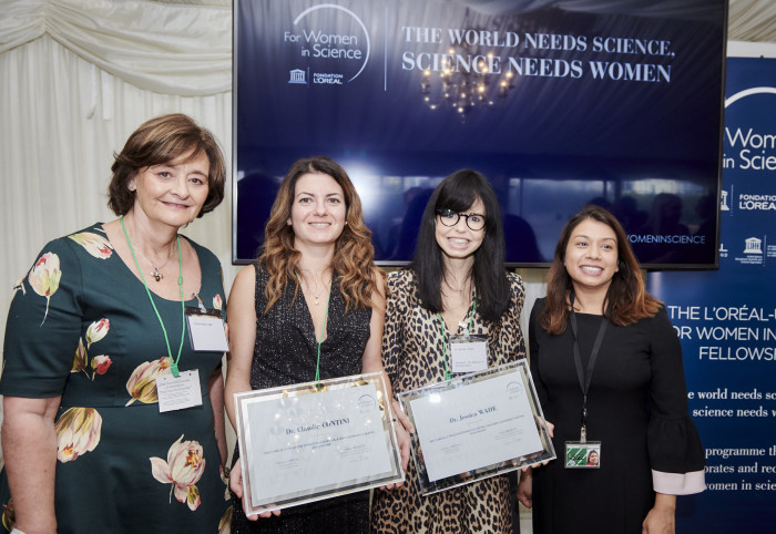 Jess Wade and Claudia Contini in front of a sign that reads 'The world needs science, science needs women'