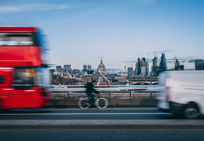 A cyclist on a bridge between a car and a bus