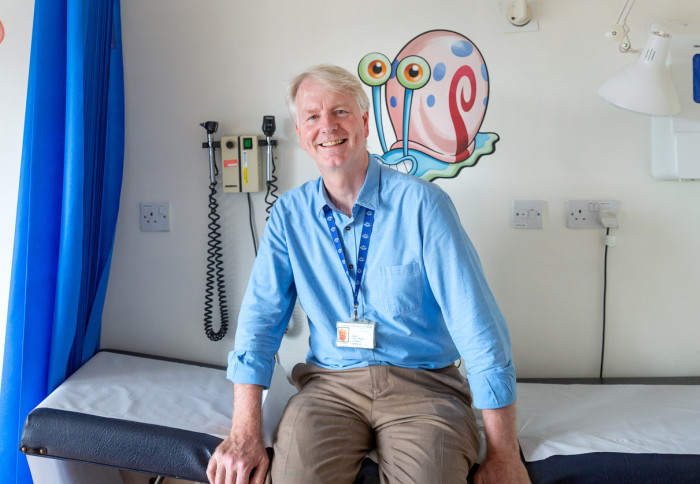 Professor Gareth Tudor-Williams sitting on a table in a paediatric clinic