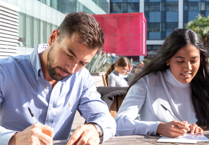 Two students sitting down outside writing on a piece of paper