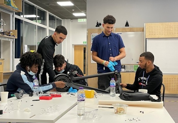 5 male teenagers behind a table looking at the e-scooter they are building