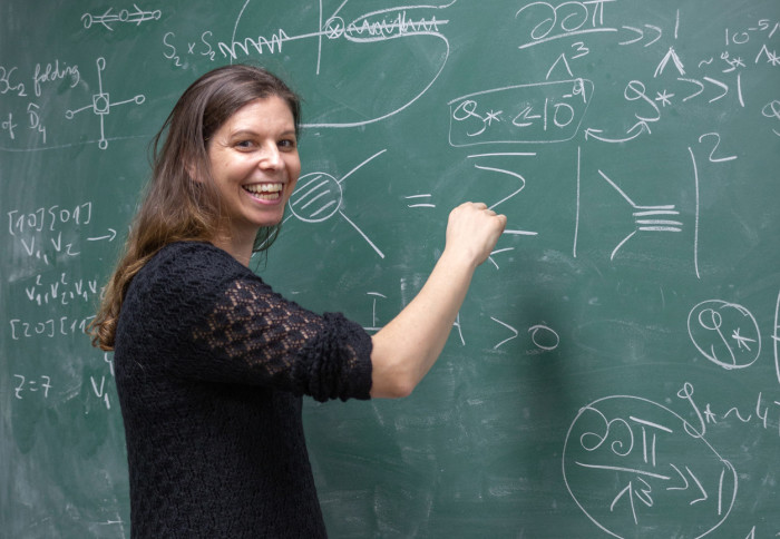 Cosmologist Claudia de Rham delivering a lecture from a blackboard full of mathematical formulae