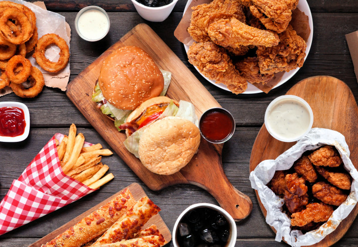 A table of fast food with burgers, chips, fried chicken and fizzy drinks.