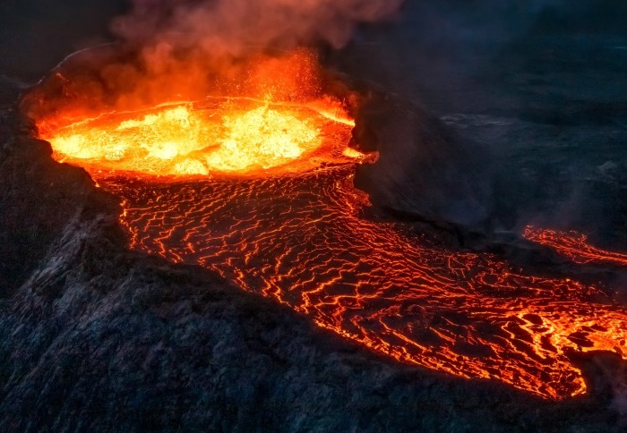 Photo of a volcano with bright orange magma erupting and spilling over the rim