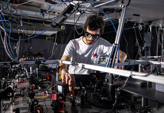 A man reaches into a complex setup of laser equipment including lenses, laser sources and wires