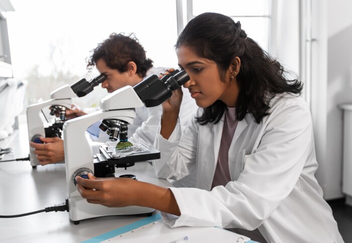 A woman in a lab coat looking down a microscope