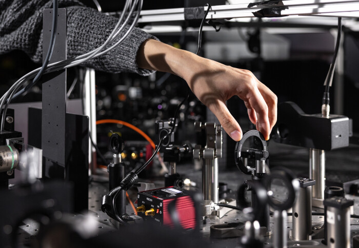 A hand, reaching to adjust a lens on a nanolasers in the ultrafast plasmonics lab. The hand belongs to 3rd year PhD student, Wai Kit Ng.