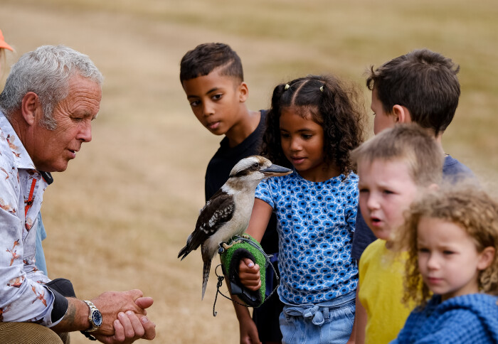 A older bird tamer monitors a younger child as they hold a kookaburra.