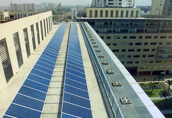 Photo shows an office block in sandstone with two rows of solar panels on the roof, it's a sunny day in the city.