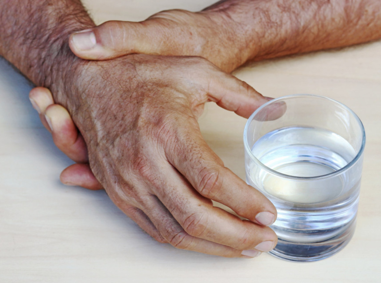 Photo depicting two older male hands holding a glass up close
