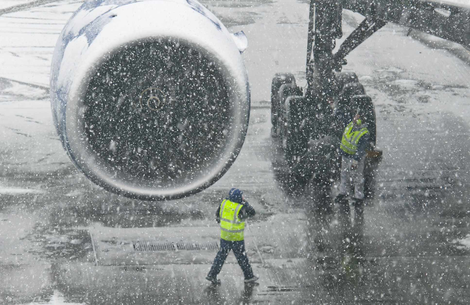 Photo of plane propeller with two airport workers during a snowstorm. Visibility is low