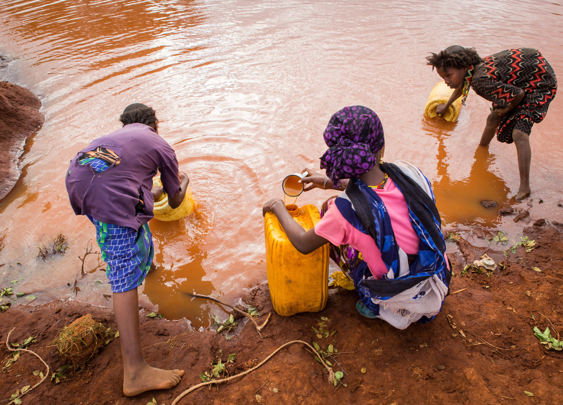 Women and young village girls collect water from a rain water pool