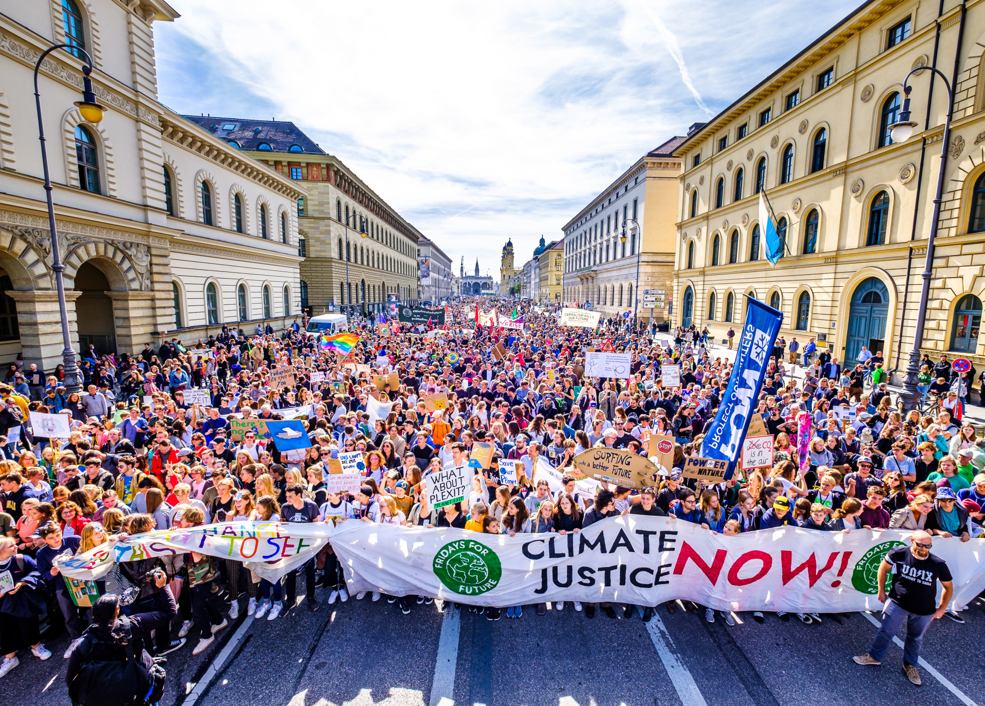 Aerial shot of a large street protest behind a banner that reads 'Climate Justice Now'