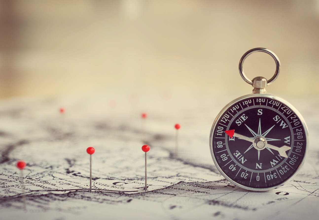 An image of a compass and map with pins in it