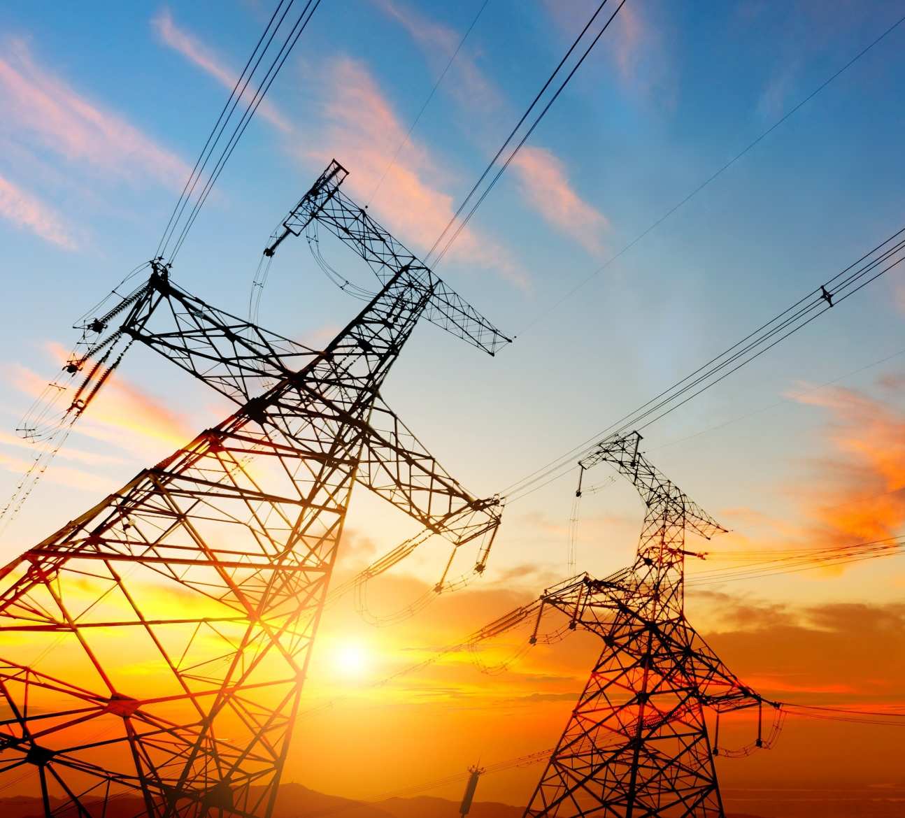 Photo of voltage tower connected to power grid, with orange sky in background