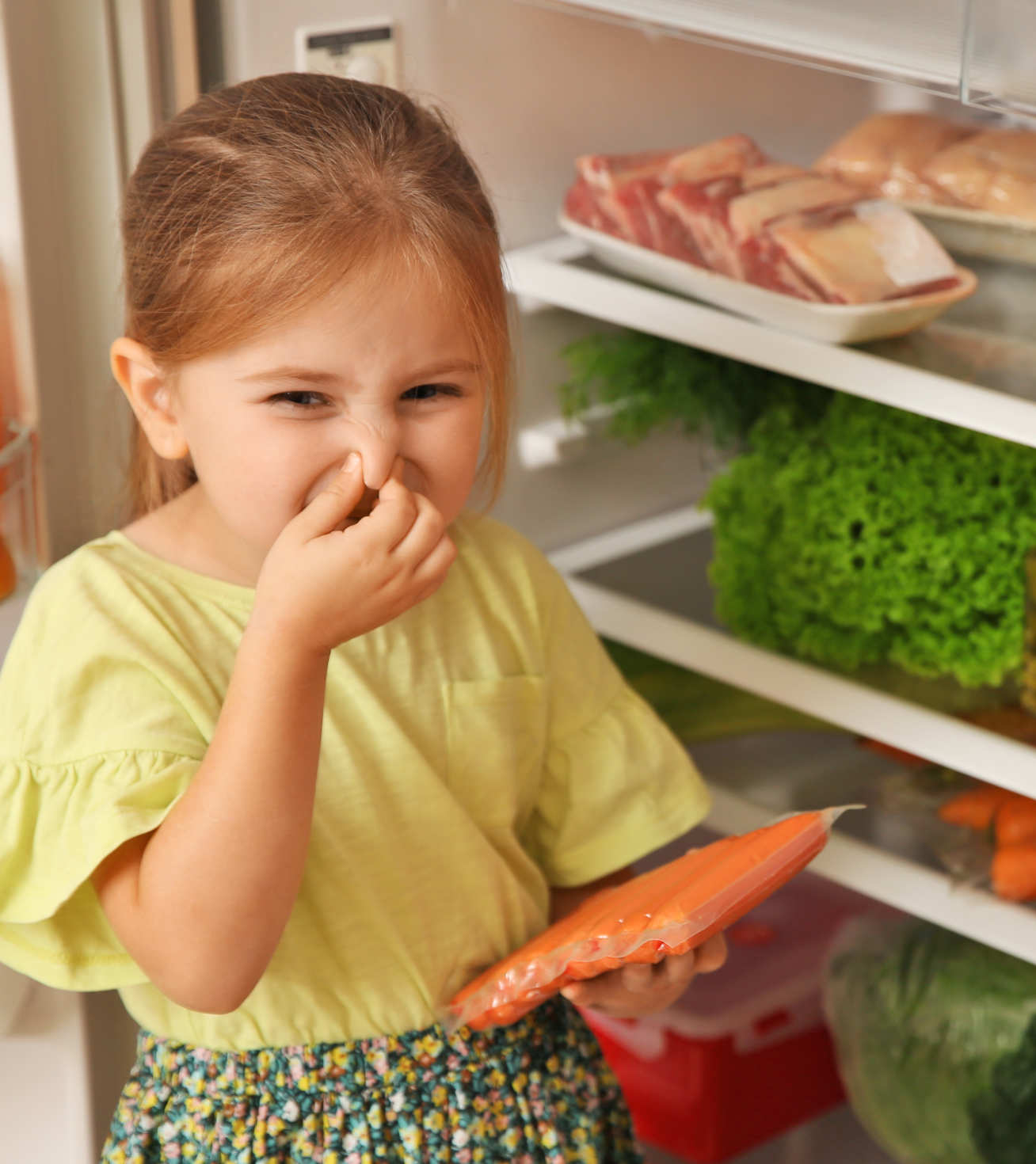 Photo of little girl next to open fridge holding a packet of sausages and pinching her nose