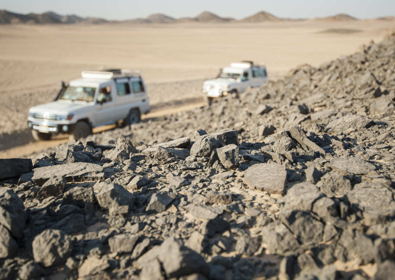 Photo of two off road vehicles travelling through a desert.