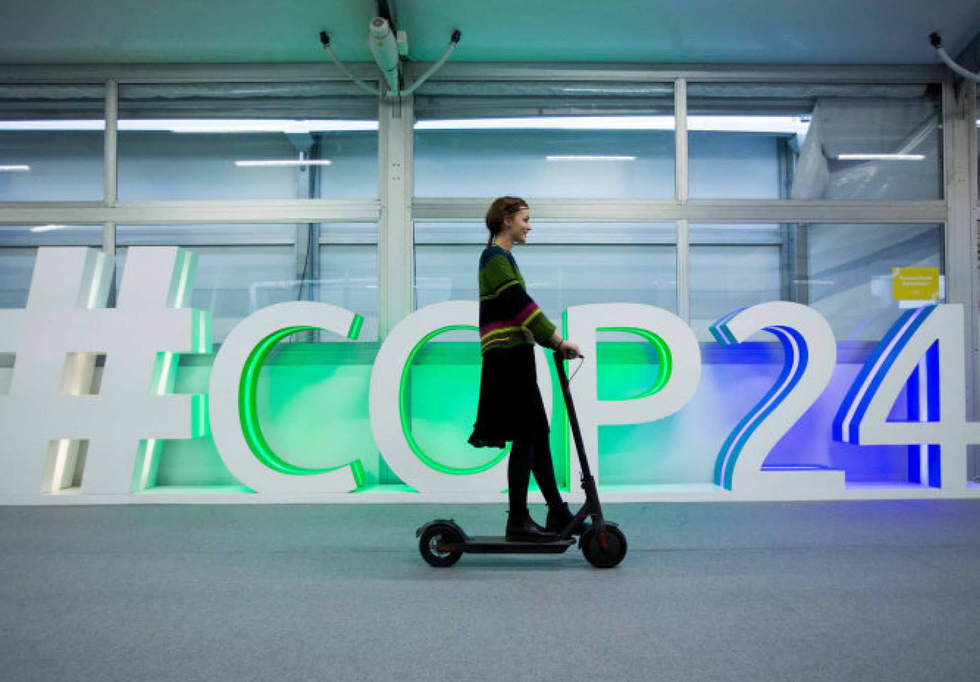 Person on a scooter going past the sign for COP24