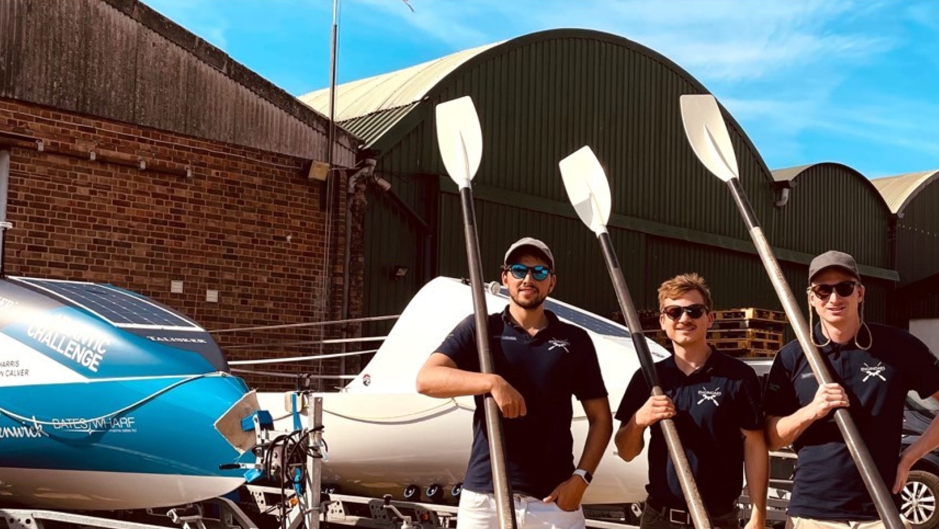 Three of the four Enginoars standing with oars outside a boating station 