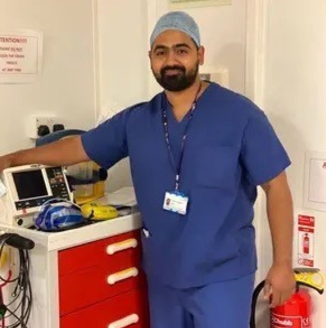 Dr Karan Rajan wearing scrubs standing with medical equipment