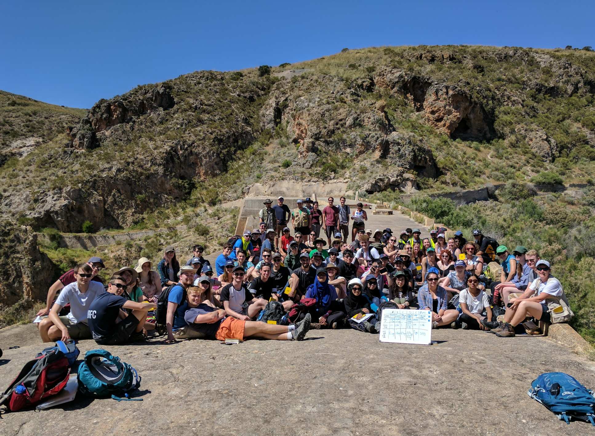 A large group of students on the 2017 Almeria field trip sit together with rocky hills in the background