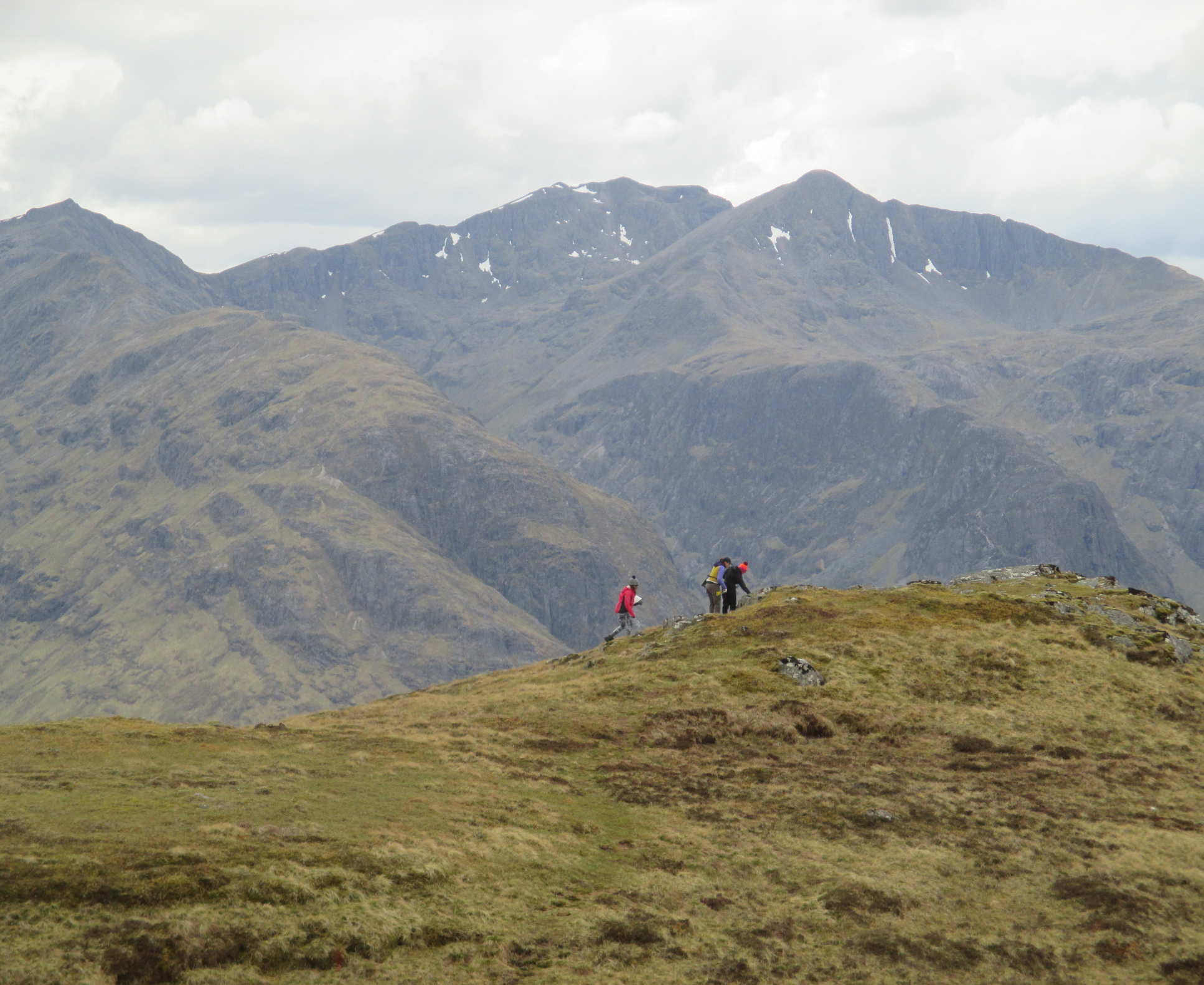 Three students walk across ridge of a mountain, with peaks in the background on a field trip to Scotland in 2017