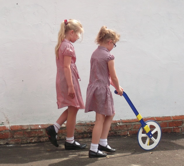 Two school pupils using a trundle wheel