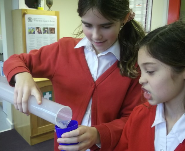 Two school students measuring water into a container