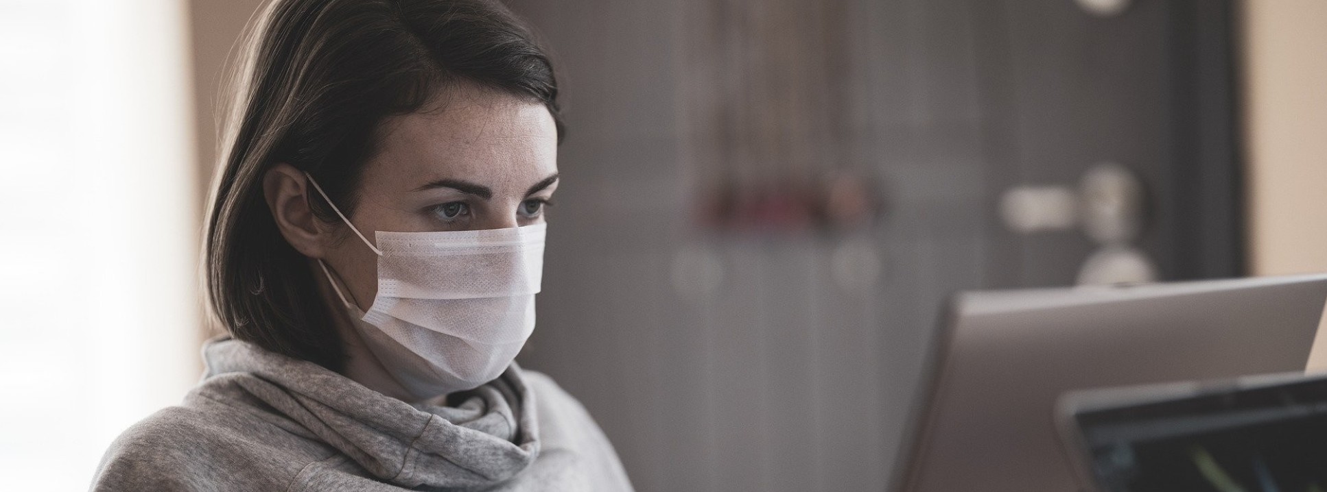 A woman working at a laptop and wearing a coronavirus mask