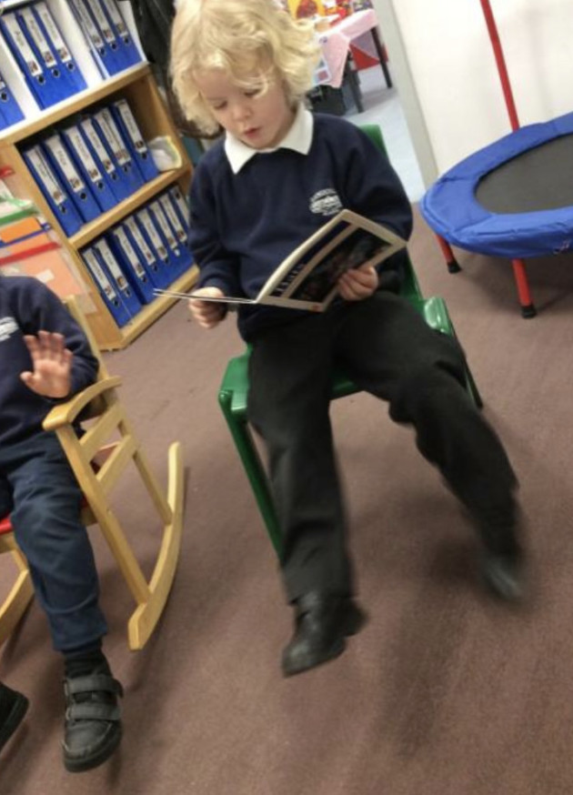 blond boy in school uniform sitting in chair, reading