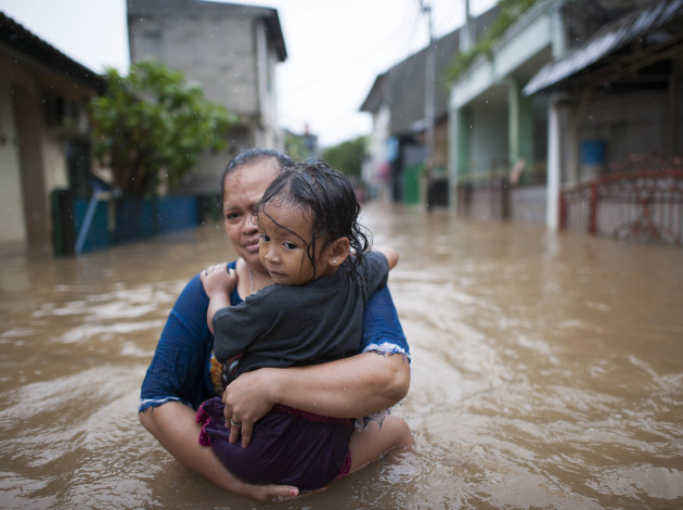 Women and child attempting to move through a flooded village. The child is clinging to the women. 