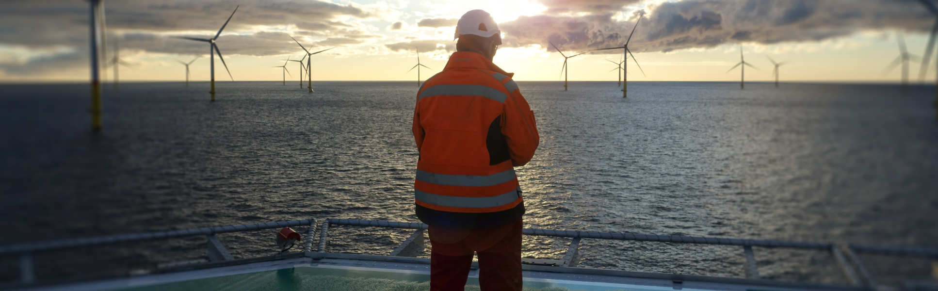 Man on a platform at sea looking out at offshore wind turbines