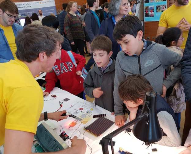 3 young boys speaking to PE-CDT student at busy science festival
