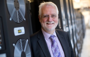 Professor Chris Hankin is standing next to a computer tower smiling