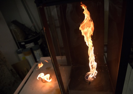 Two identical dishes of ignited liquid fuel, with the right one in a simple enclosure with asymetic air slots