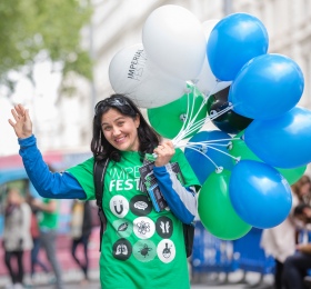 A female Festival volunteers holds balloons and waves at the camera