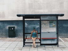 Emma sits at a bus stop, wearing her swimming costume, cap and goggles