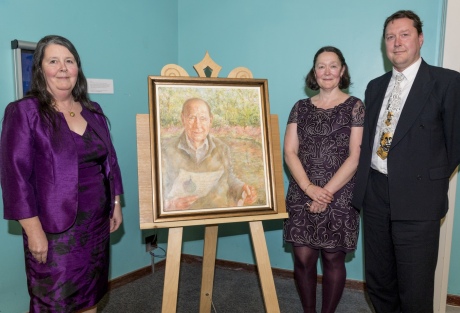 Three people standing around an unveiled portrait