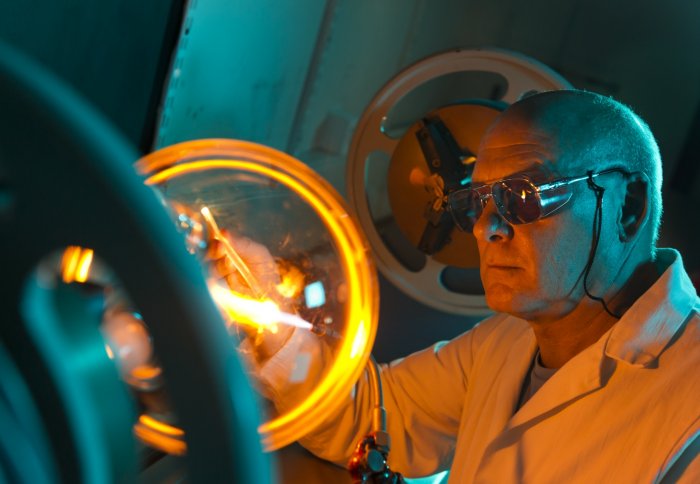 Man in labcoat and dark glasses with yellow-hot glass