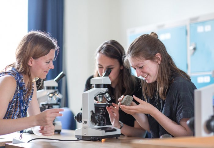 teaching staff and two students looking at rocks with microscope