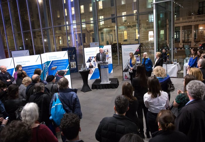 man standing at podium in front of standing audience with large exhibition panels in background