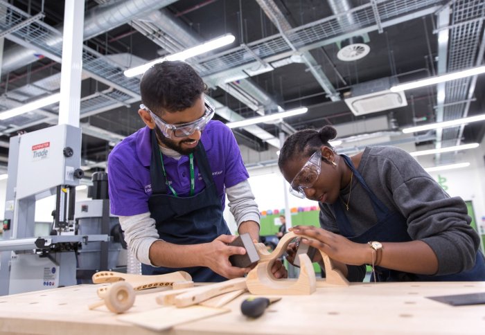 Two students wearing safety goggles sanding a wooden object in the workshop