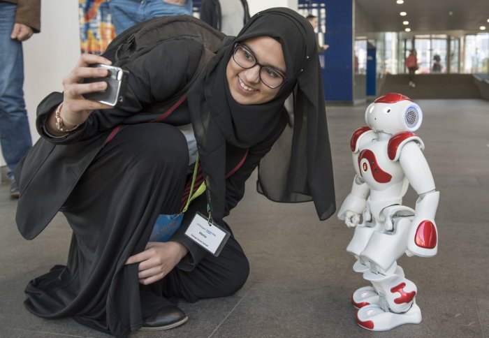A female visiting school student takes a selfie with a small white and red robot