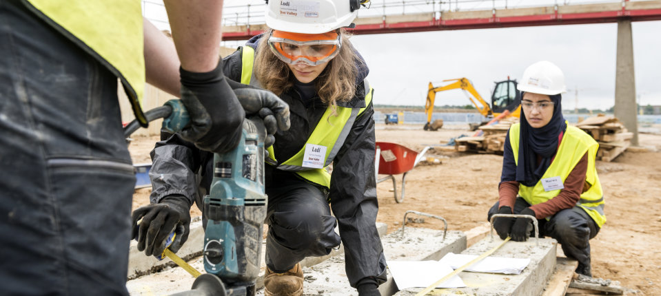 Two students in high vis jackets and helmets working on an outdoor civil engineering projects