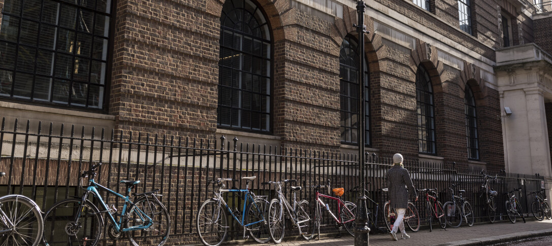 Bikes placed against railings outside St Mary's Hospital Medical School building as a woman walks past them wearing a winter coat and hat 