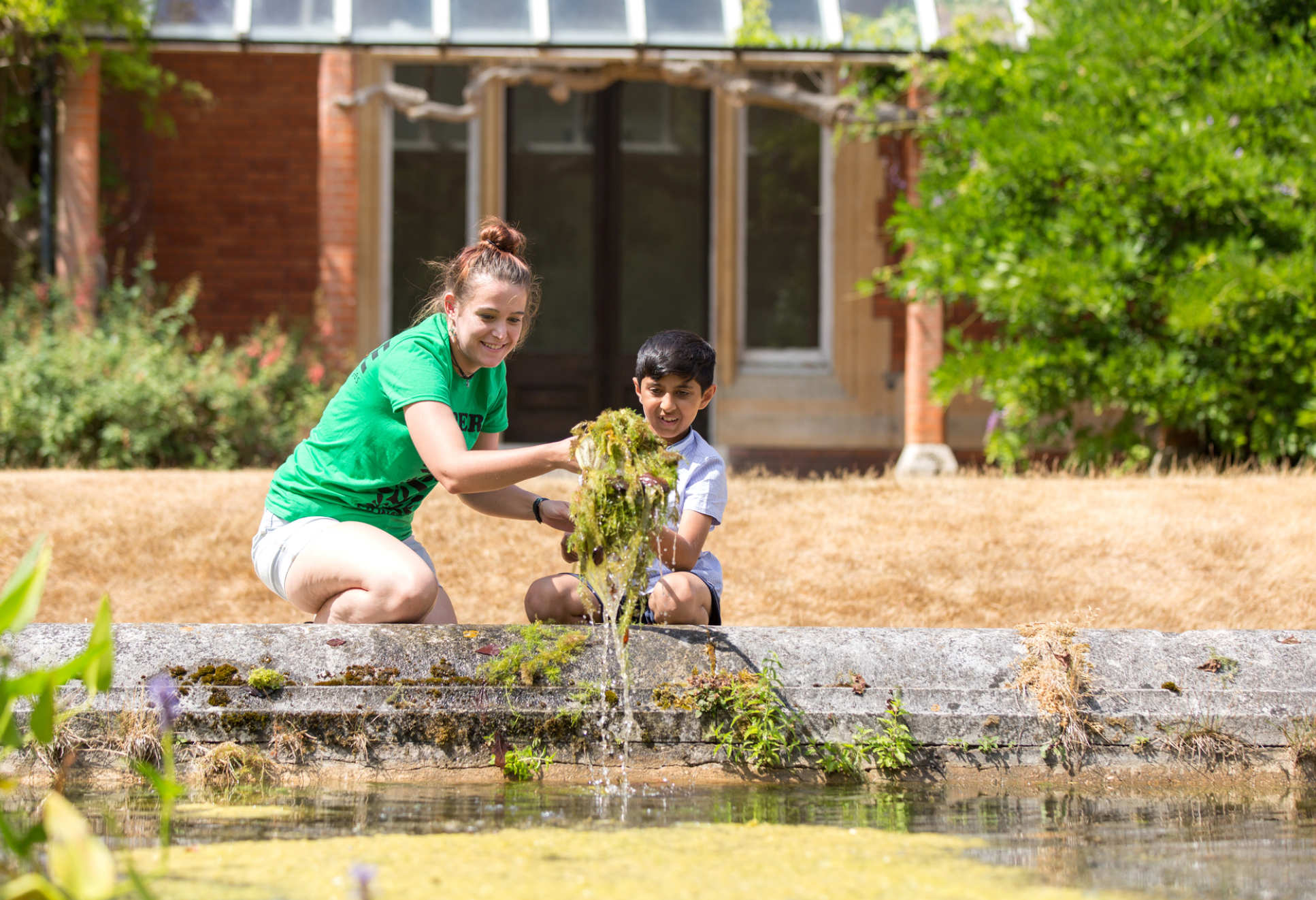 A woman and child pull pondweed from a pond