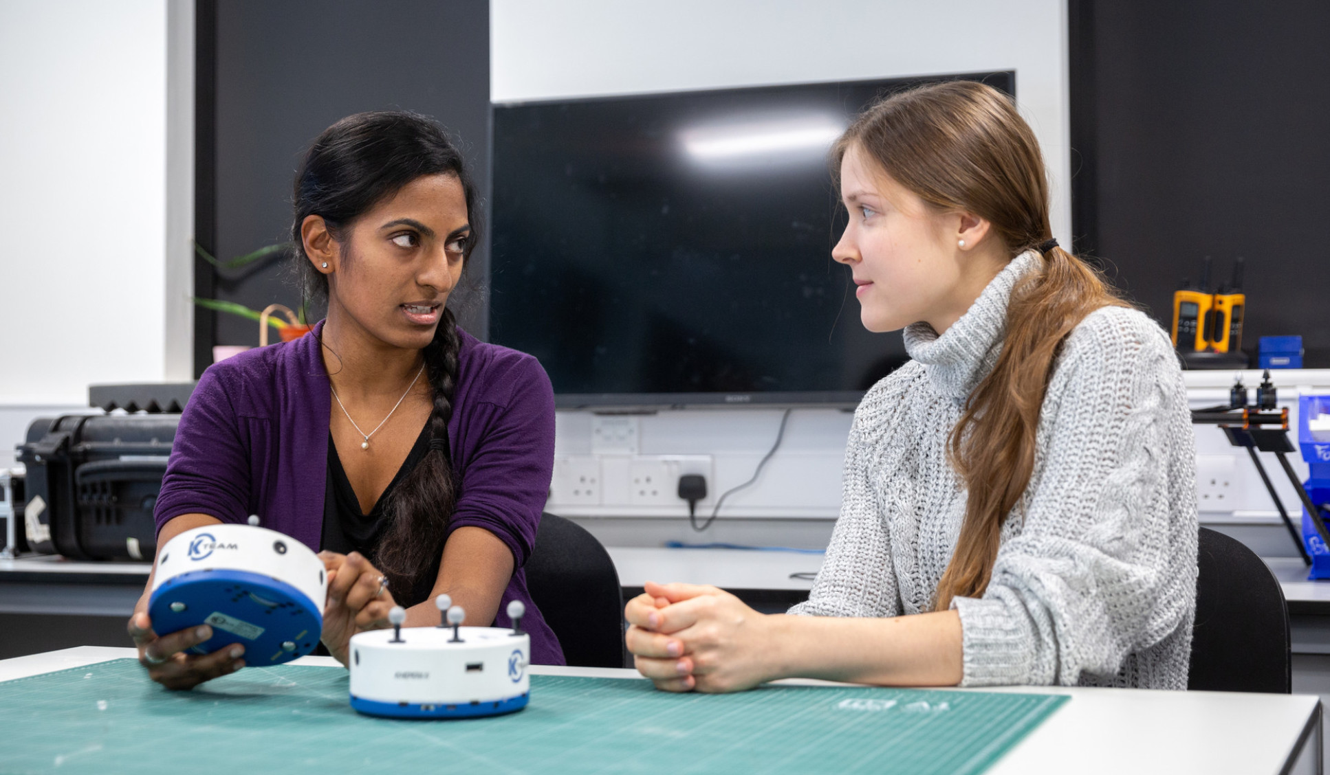 two women sitting at table with equipment talking